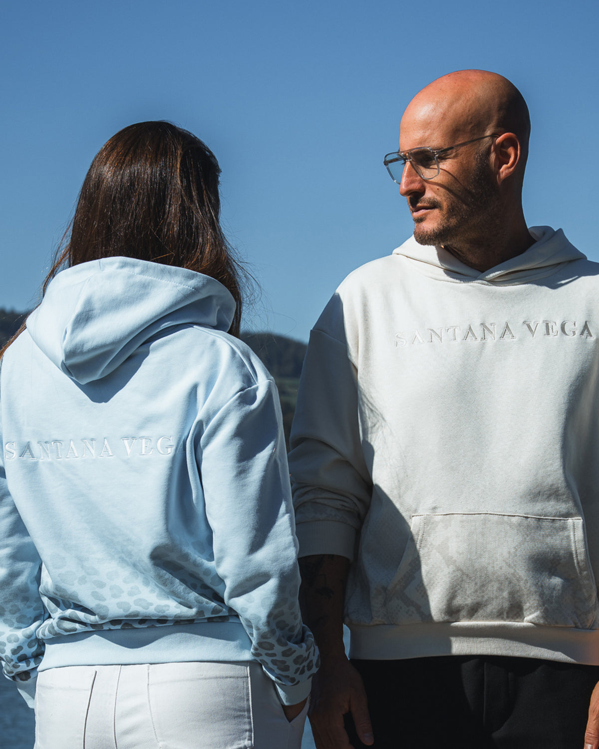 Frau im hellblauen Leopard Hoodie und Mann im Off-White Snake Hoodie von Santana Vega mit Schriftzug auf der Brust